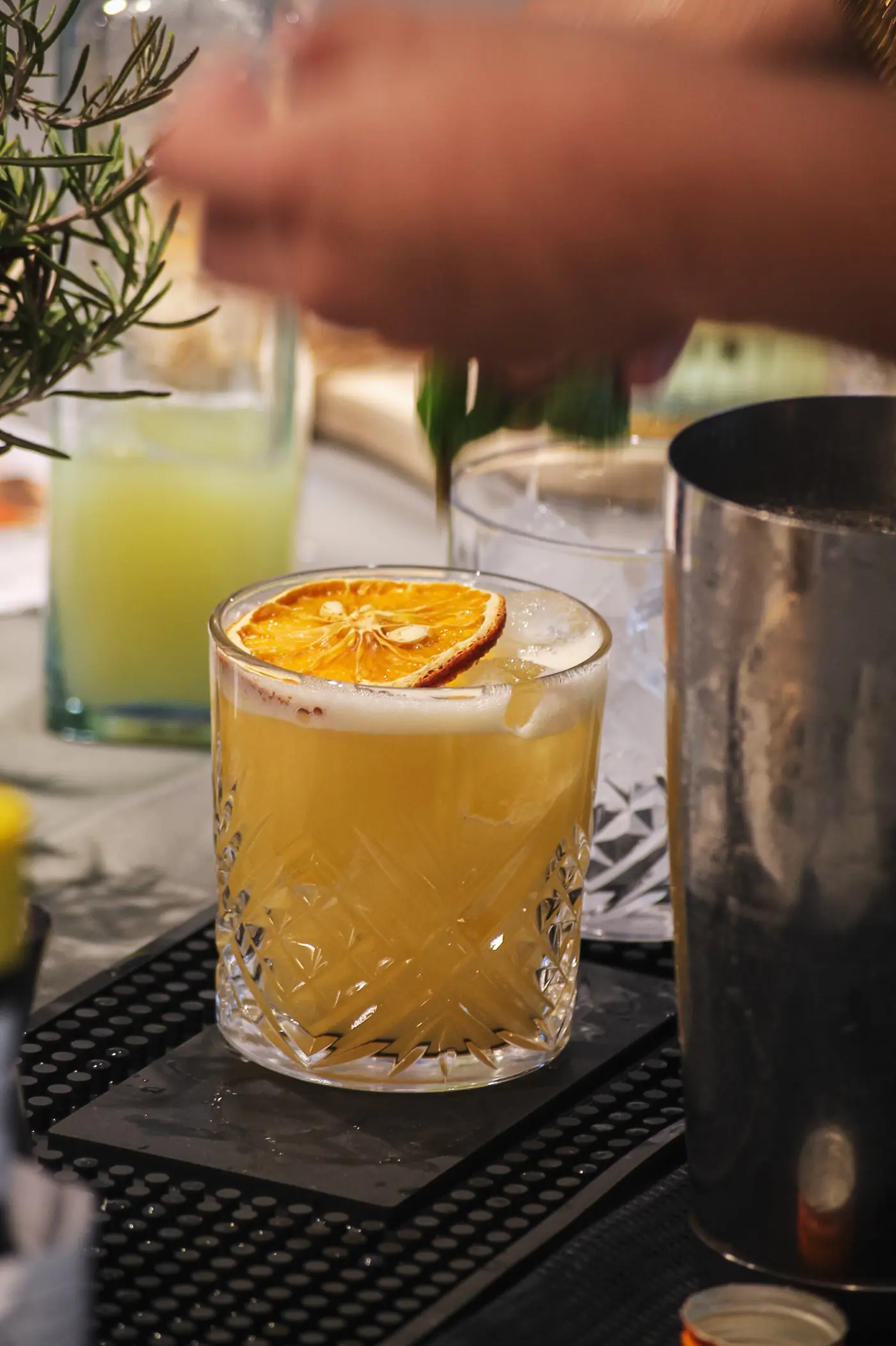 Cocktail dressé sur le bar, shaker et branches de romarin à côté