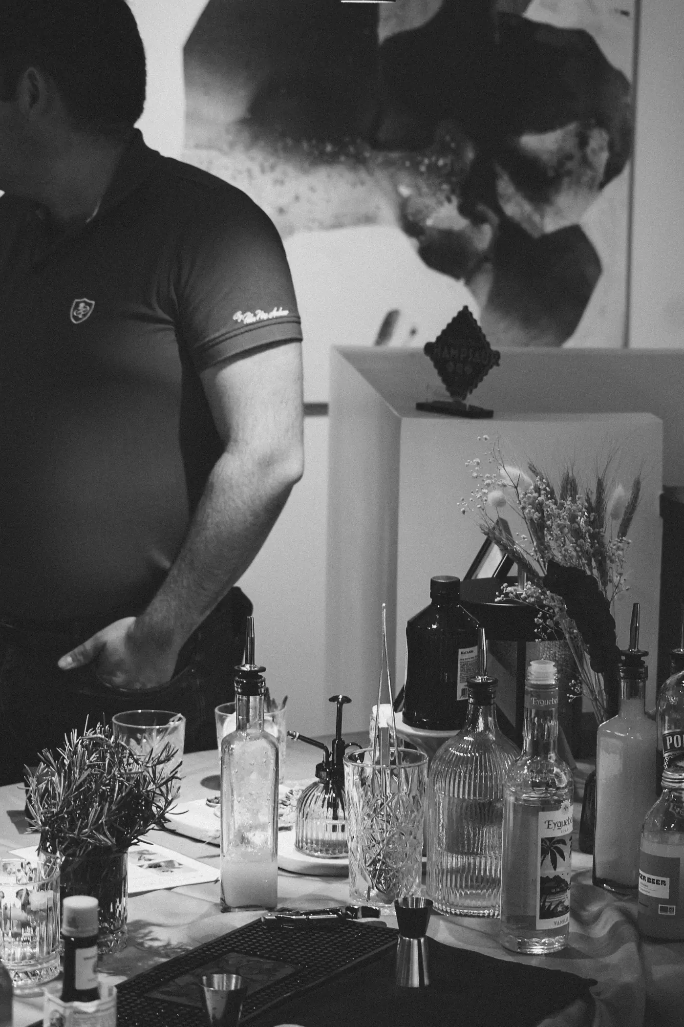 Lucile, créateur de cocktails, derrière son bar mobile, bouteilles et herbes fraîches, photo noir et blanc